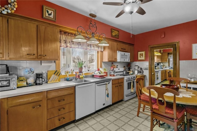 kitchen with brown cabinets, light countertops, a sink, ceiling fan, and white appliances