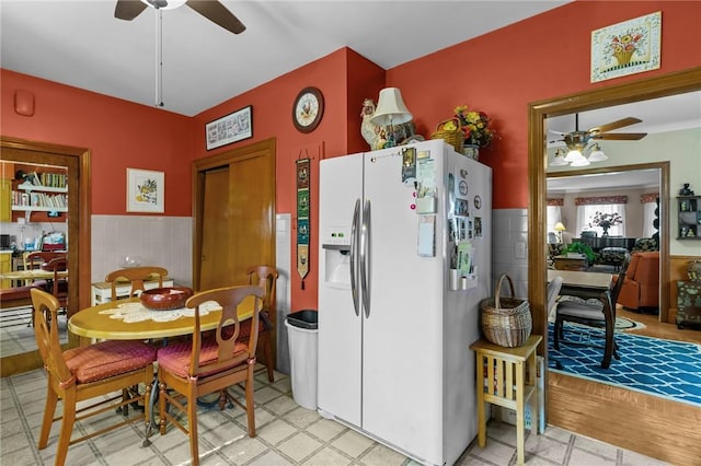 kitchen featuring white fridge with ice dispenser, a wainscoted wall, tile walls, and a ceiling fan