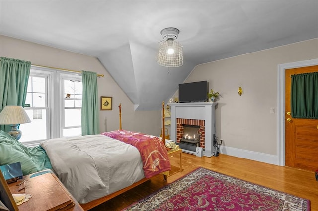 bedroom with lofted ceiling, a brick fireplace, baseboards, and wood finished floors