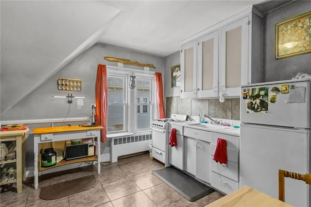 kitchen featuring white appliances, light tile patterned floors, radiator heating unit, white cabinetry, and a sink