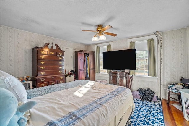 bedroom with wallpapered walls, ceiling fan, a textured ceiling, and wood finished floors