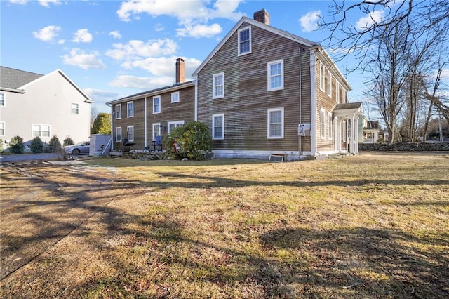 back of house featuring a lawn and a chimney