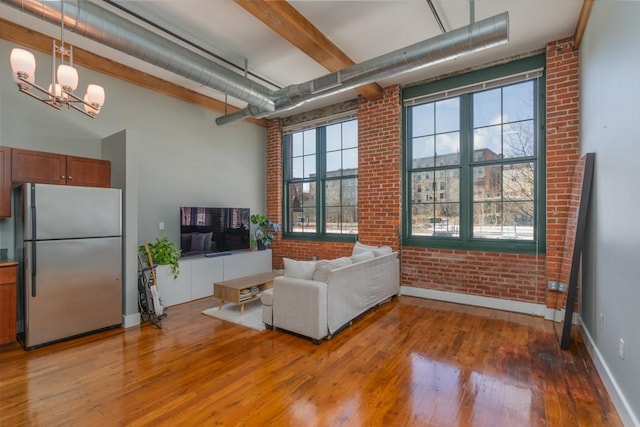 living room with an inviting chandelier, a towering ceiling, hardwood / wood-style flooring, and brick wall