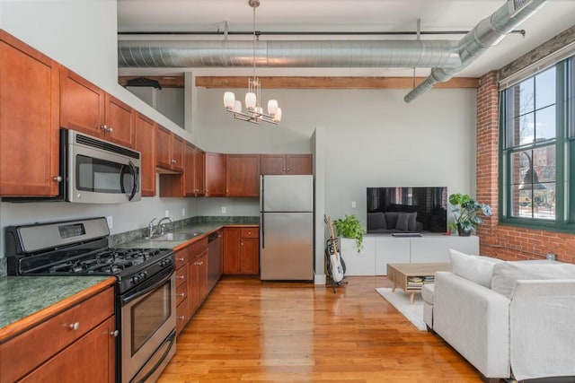 kitchen featuring brick wall, appliances with stainless steel finishes, pendant lighting, sink, and a notable chandelier