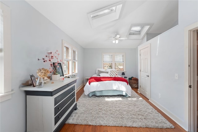 bedroom featuring ceiling fan, vaulted ceiling with skylight, light wood-type flooring, and baseboards