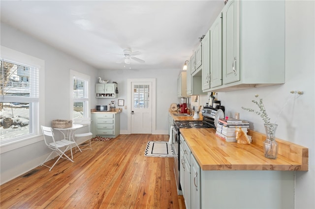 kitchen featuring wooden counters, a ceiling fan, stainless steel range with electric cooktop, a sink, and light wood-type flooring