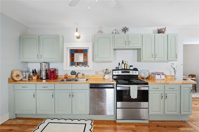 kitchen featuring stainless steel appliances, a sink, a ceiling fan, baseboards, and light wood finished floors