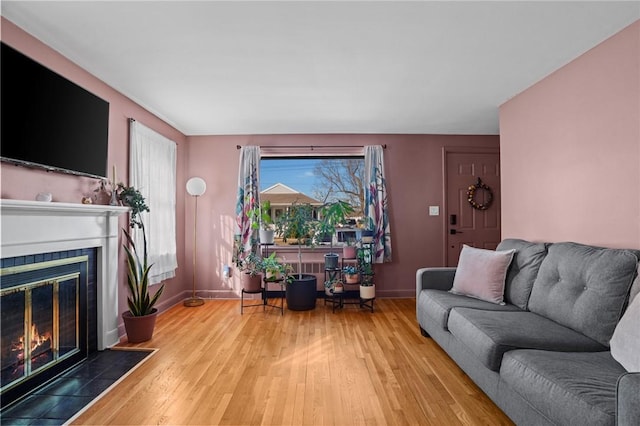 living area with baseboards, wood finished floors, and a tile fireplace