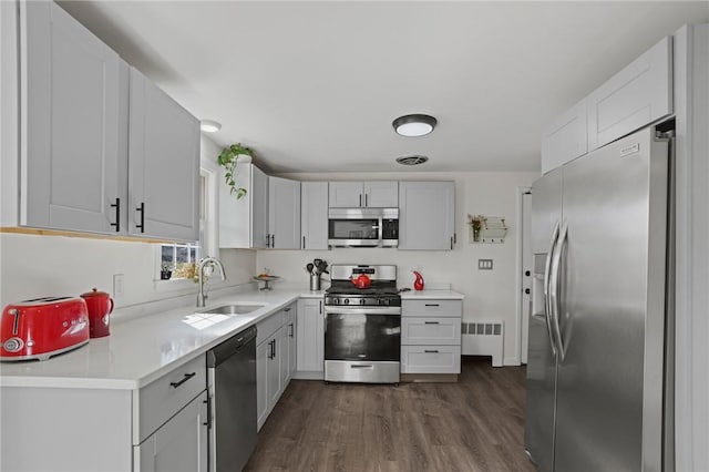 kitchen featuring dark wood-type flooring, a sink, radiator heating unit, appliances with stainless steel finishes, and light countertops