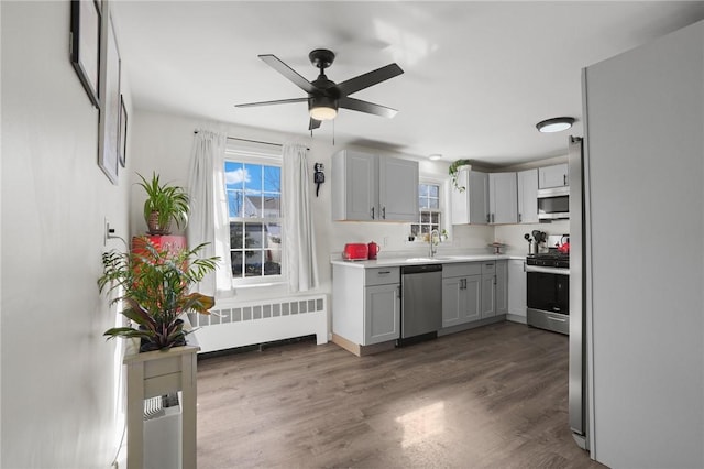 kitchen with a sink, wood finished floors, stainless steel appliances, radiator, and light countertops