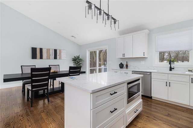 kitchen with sink, a center island, appliances with stainless steel finishes, light stone countertops, and white cabinets