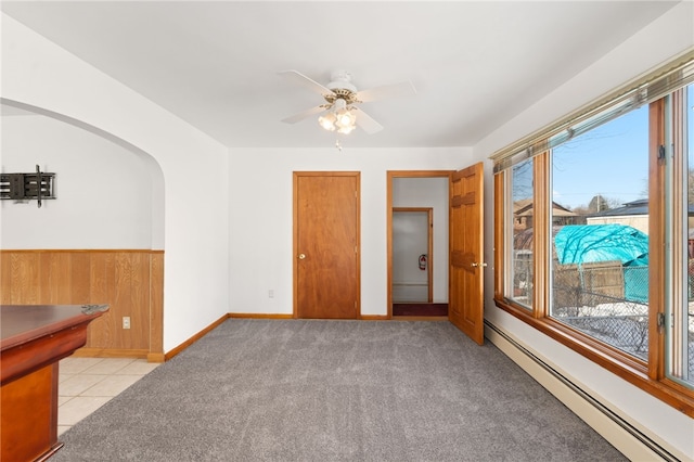 unfurnished room with light carpet, baseboard heating, ceiling fan, and wood walls