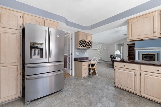 kitchen with a fireplace, vaulted ceiling, light brown cabinetry, dark countertops, and stainless steel fridge