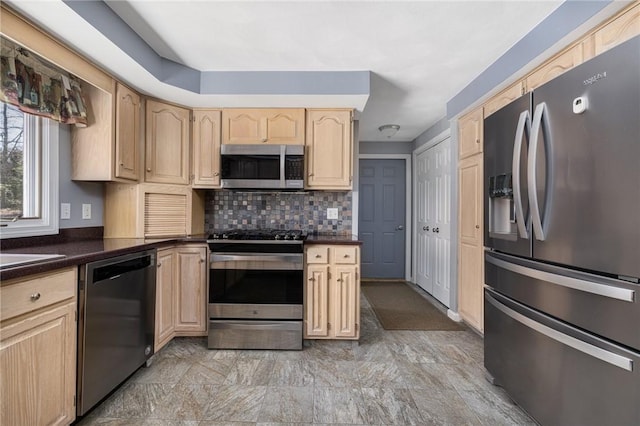 kitchen featuring dark countertops, appliances with stainless steel finishes, decorative backsplash, and light brown cabinetry