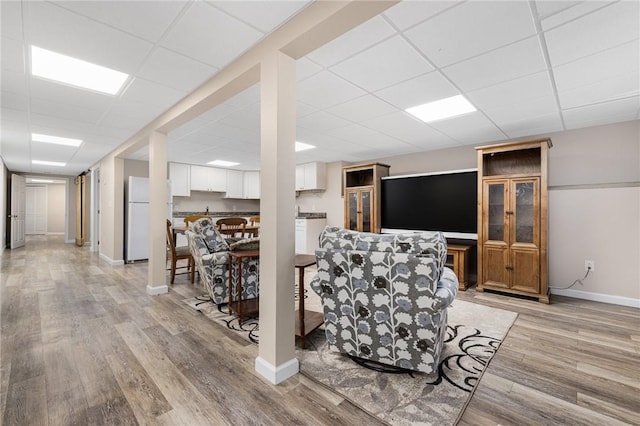 living room with a drop ceiling, light wood-type flooring, and baseboards