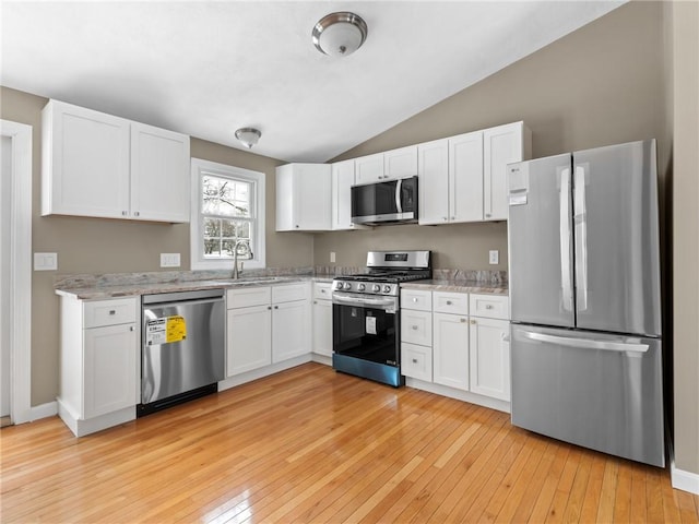 kitchen with appliances with stainless steel finishes, light stone counters, white cabinets, vaulted ceiling, and sink