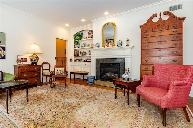 living area featuring a premium fireplace, light hardwood / wood-style flooring, crown molding, and built in features