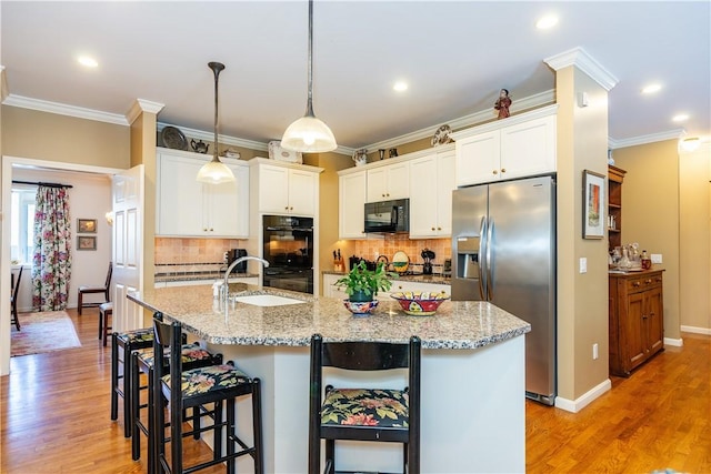 kitchen featuring black appliances, decorative light fixtures, sink, white cabinetry, and a kitchen island with sink