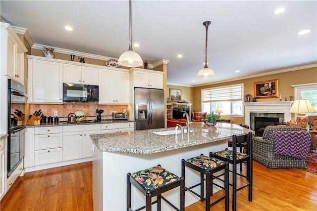 kitchen featuring a center island with sink, hanging light fixtures, black appliances, sink, and a breakfast bar area