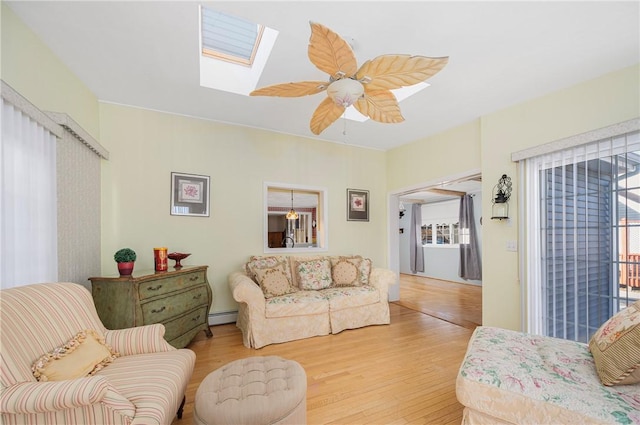 living room with ceiling fan, baseboard heating, wood-type flooring, and a skylight