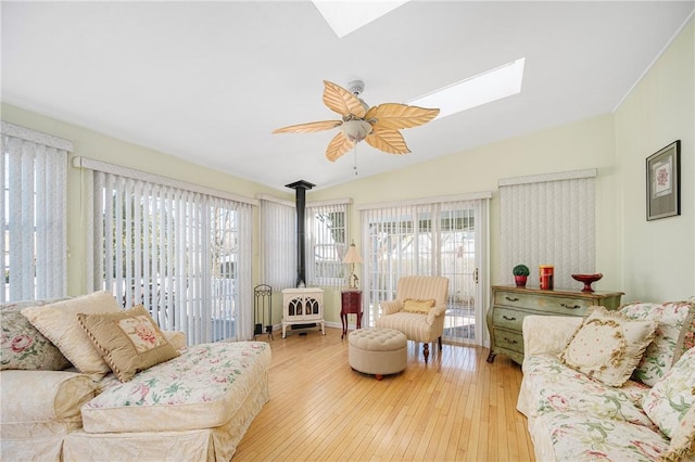 living room featuring plenty of natural light, light hardwood / wood-style floors, a wood stove, and vaulted ceiling with skylight