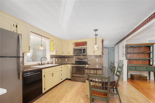 kitchen with sink, pendant lighting, light hardwood / wood-style floors, stainless steel appliances, and cream cabinets