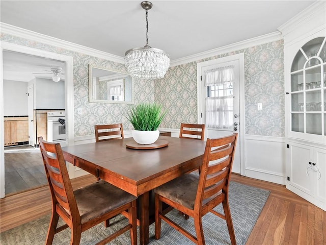 dining space with hardwood / wood-style flooring, crown molding, and ceiling fan with notable chandelier