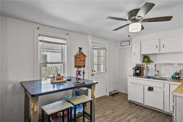 kitchen with white cabinetry, light hardwood / wood-style floors, sink, ceiling fan, and decorative backsplash