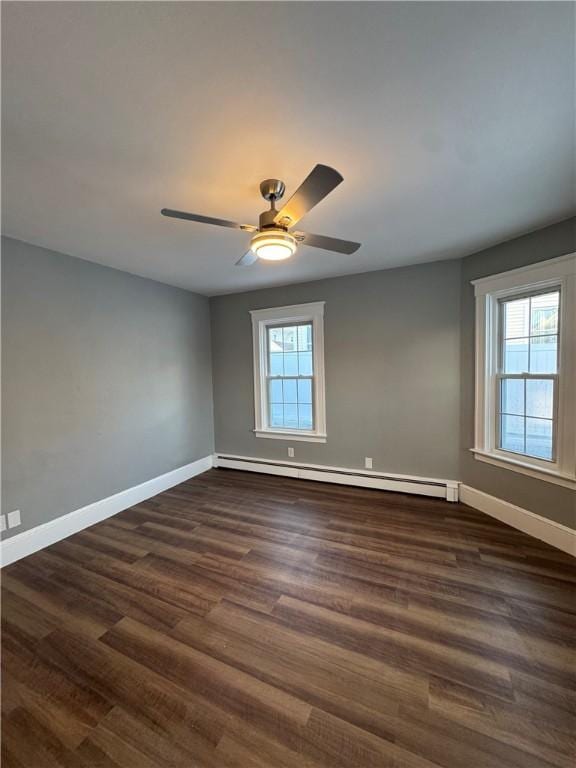 empty room featuring a baseboard heating unit, ceiling fan, dark hardwood / wood-style floors, and a wealth of natural light