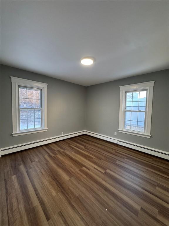 empty room with dark wood-type flooring, a baseboard radiator, and a wealth of natural light