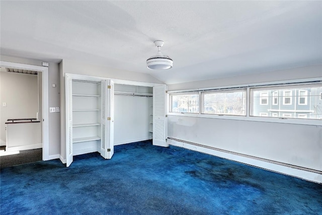 unfurnished bedroom with a baseboard heating unit, vaulted ceiling, and dark carpet