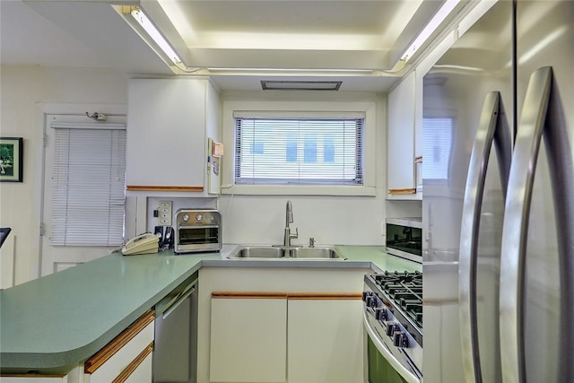 kitchen with appliances with stainless steel finishes, sink, white cabinetry, and kitchen peninsula