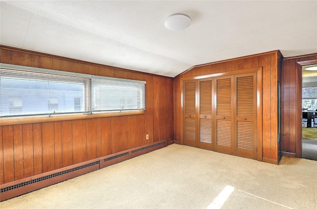 unfurnished bedroom with a closet, vaulted ceiling, wood walls, a baseboard radiator, and light colored carpet