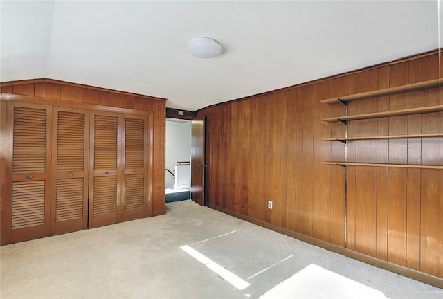 unfurnished bedroom featuring light carpet, wooden walls, and a closet