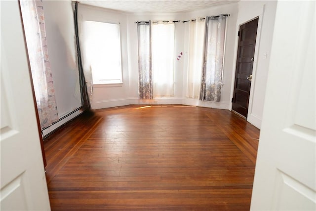 unfurnished room with dark wood-type flooring and a baseboard radiator