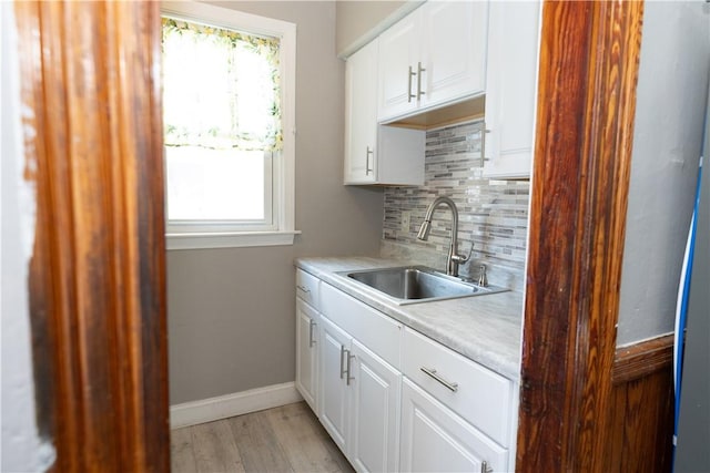 kitchen featuring sink, white cabinetry, light wood-type flooring, and decorative backsplash