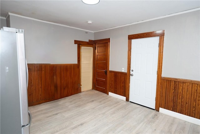 empty room featuring ornamental molding, light hardwood / wood-style floors, and wood walls