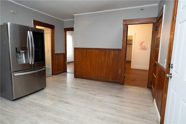 kitchen with ornamental molding, light wood-type flooring, wood walls, and stainless steel fridge