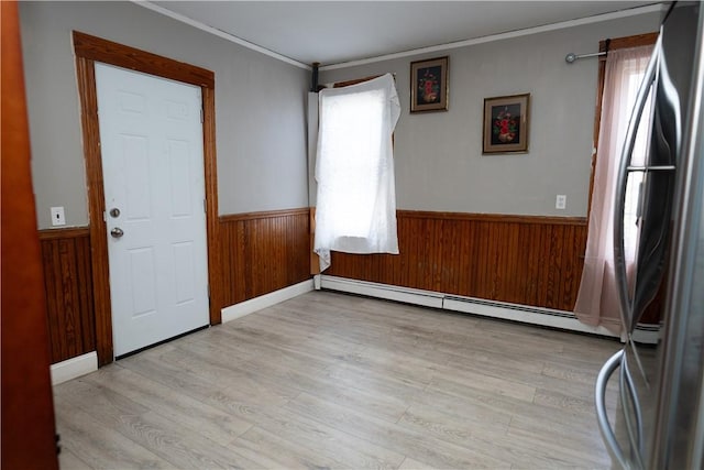 empty room featuring baseboard heating, light hardwood / wood-style floors, and wood walls