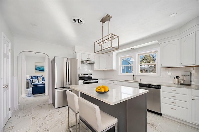 kitchen with appliances with stainless steel finishes, decorative light fixtures, backsplash, a kitchen island, and white cabinetry