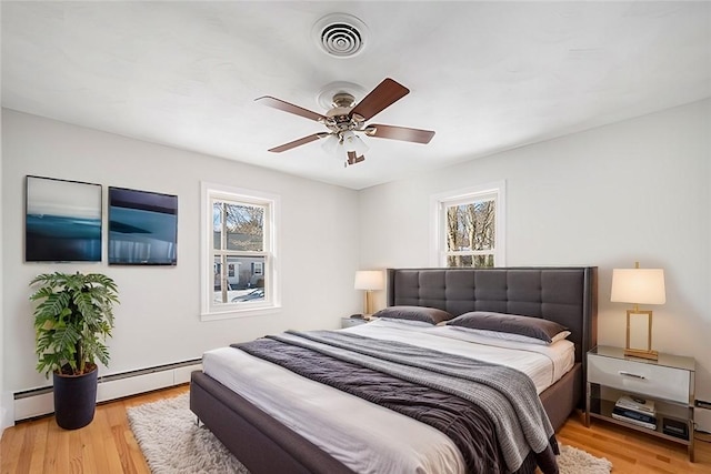 bedroom featuring light wood-type flooring, ceiling fan, and a baseboard heating unit