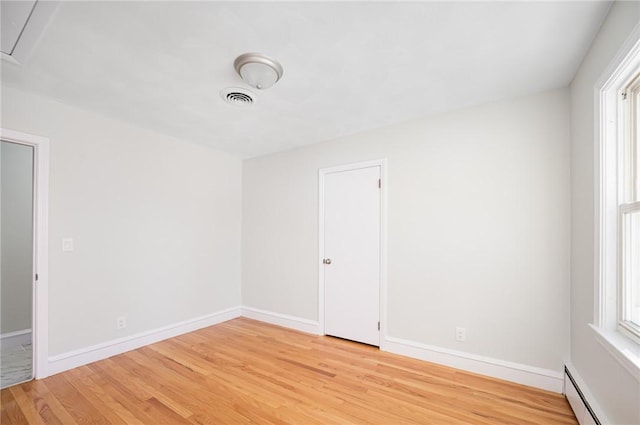 unfurnished room with a baseboard heating unit, light hardwood / wood-style floors, and plenty of natural light