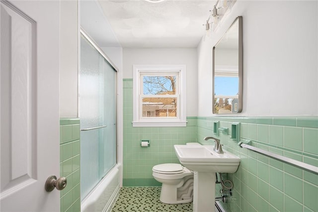 bathroom featuring tile walls, toilet, and enclosed tub / shower combo