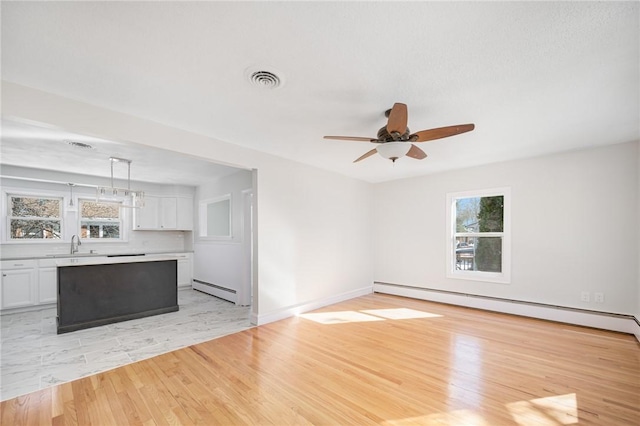 interior space with a baseboard heating unit, sink, light wood-type flooring, and ceiling fan