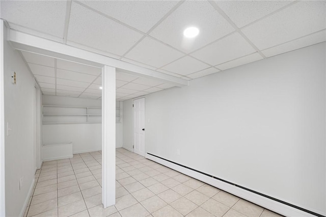 basement with a baseboard radiator, a paneled ceiling, and light tile patterned flooring