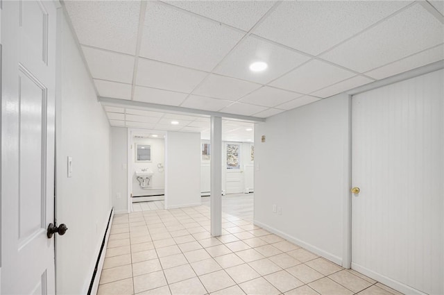 basement with light tile patterned flooring, a drop ceiling, and a baseboard radiator