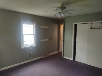 unfurnished bedroom featuring dark carpet, a closet, a wall mounted air conditioner, a ceiling fan, and baseboards