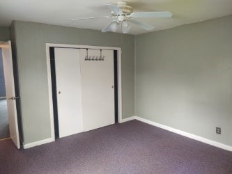 unfurnished bedroom featuring dark colored carpet, a closet, baseboards, and ceiling fan