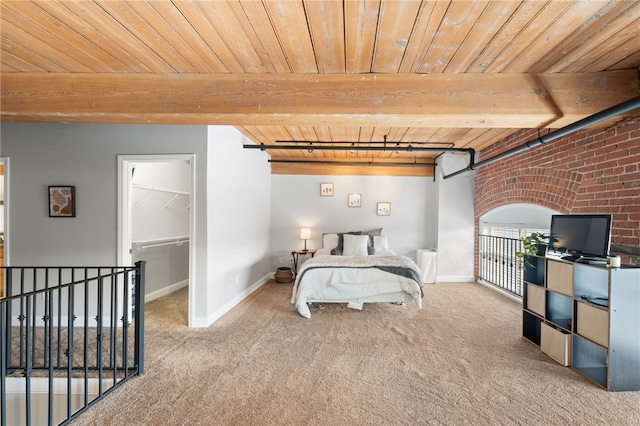 carpeted bedroom with brick wall, wooden ceiling, a spacious closet, and beam ceiling