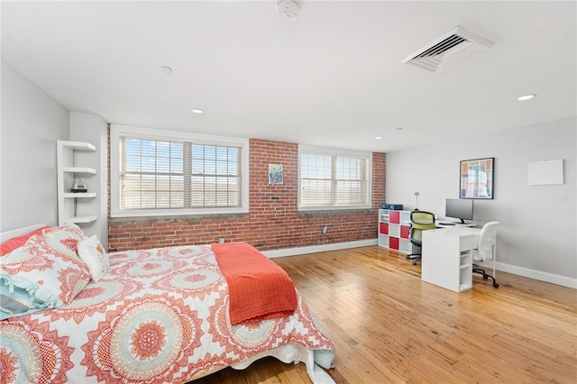 bedroom with light hardwood / wood-style floors and brick wall